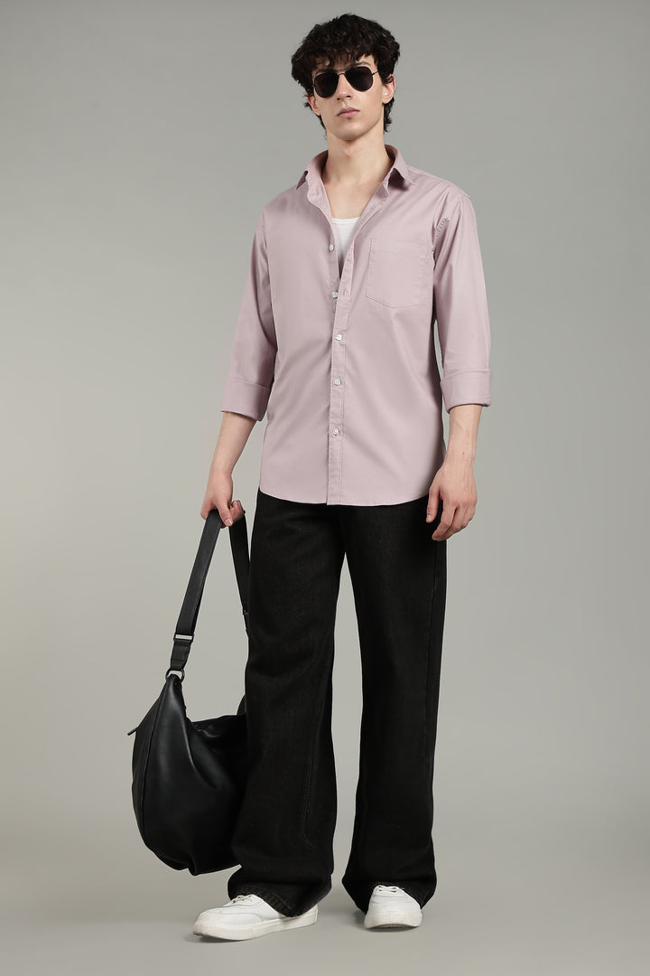 Man wearing a mute pink shirt, black pants, and sunglasses, holding a black bag on a gray background