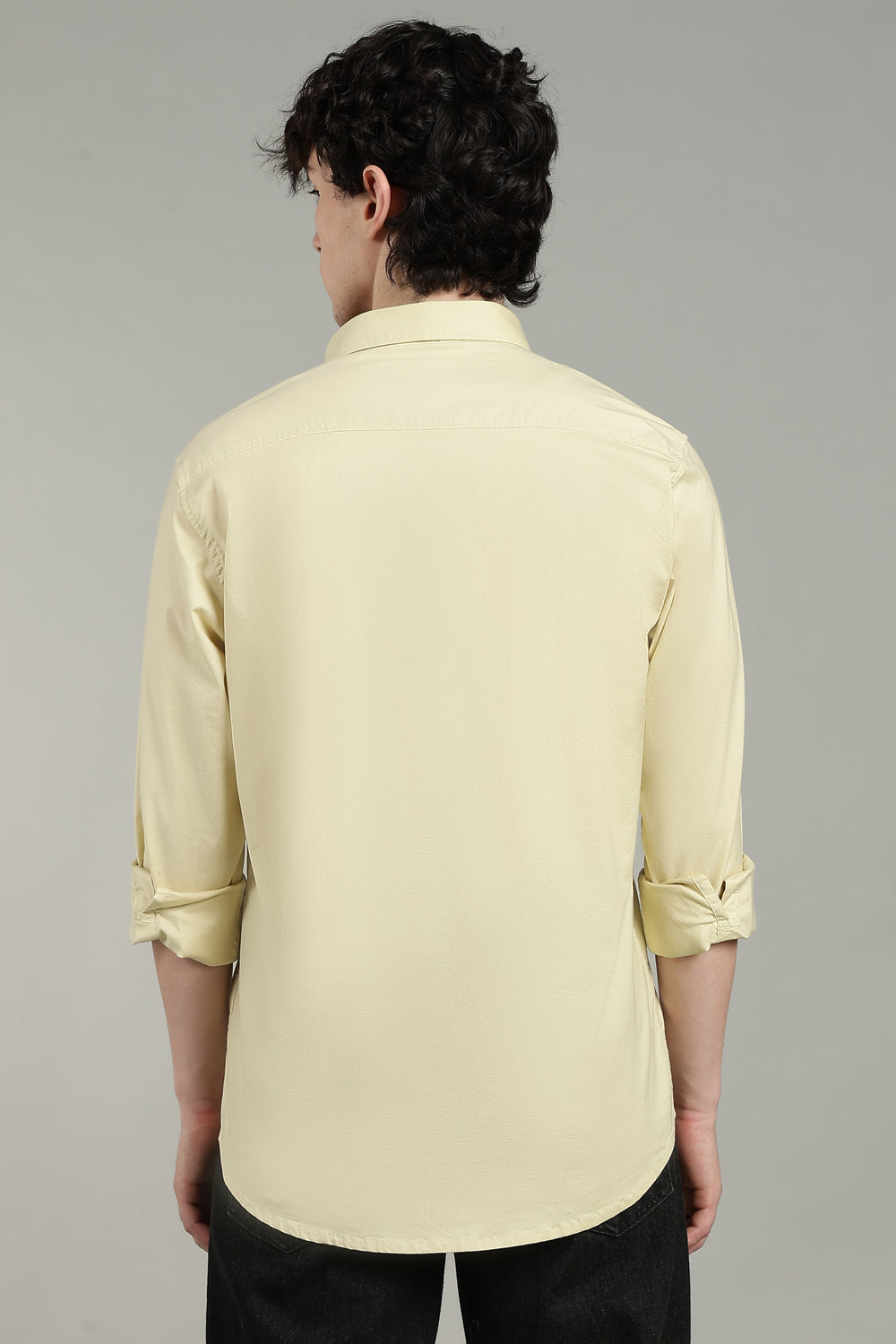 man wearing a light yellow shirt with rolled-up sleeves on a gray background