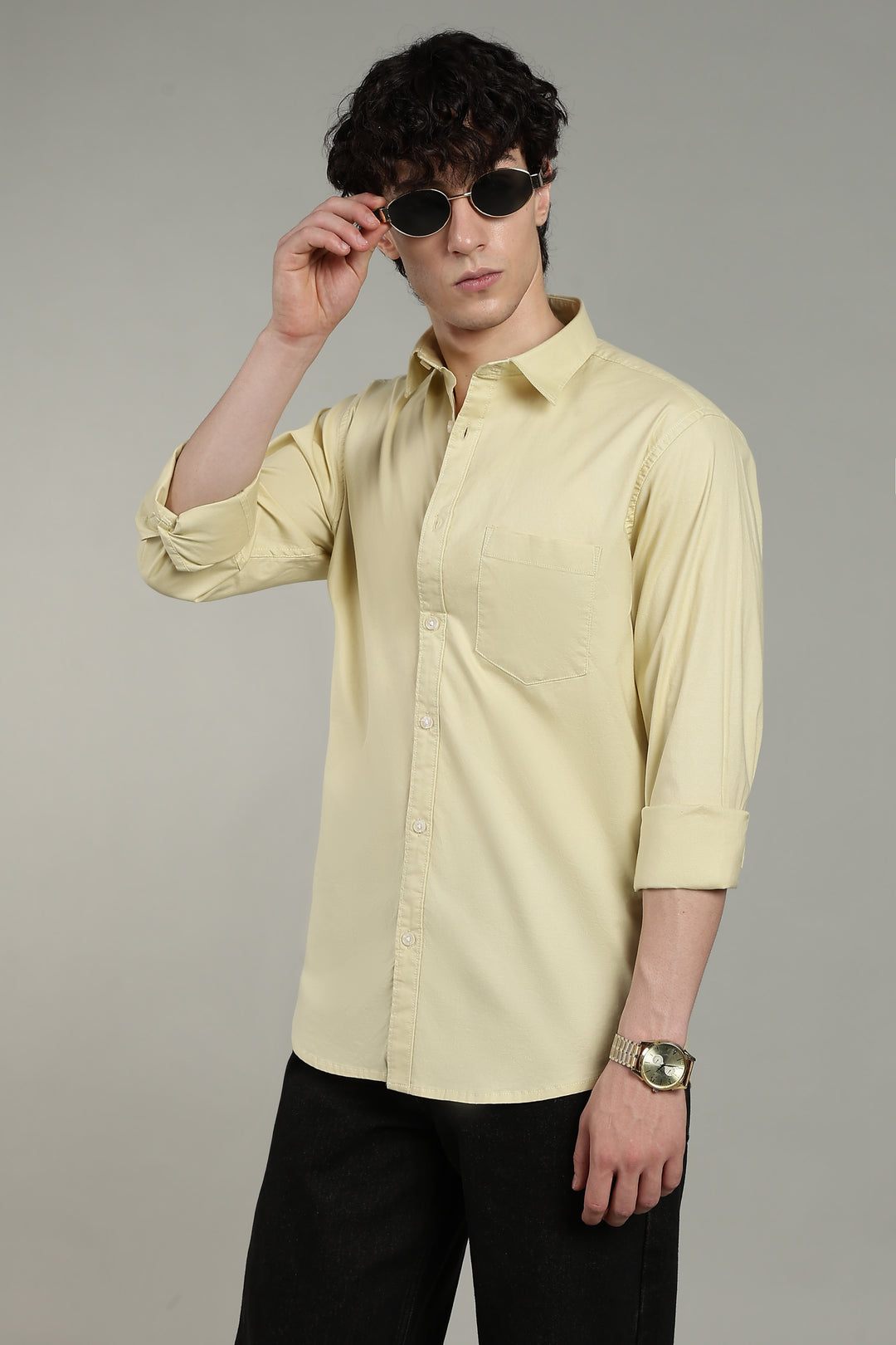Man wearing a light yellow shirt and black pants against a gray background
