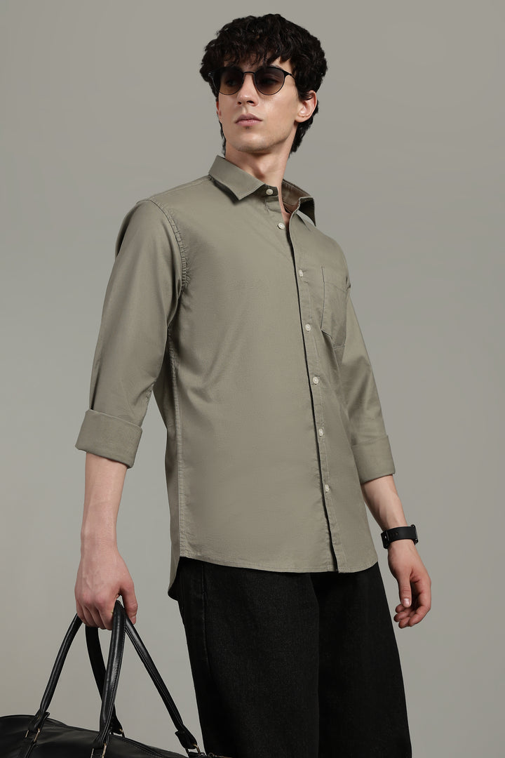 Man wearing a sage green shirt and black pants, holding a suitcase against a gray background