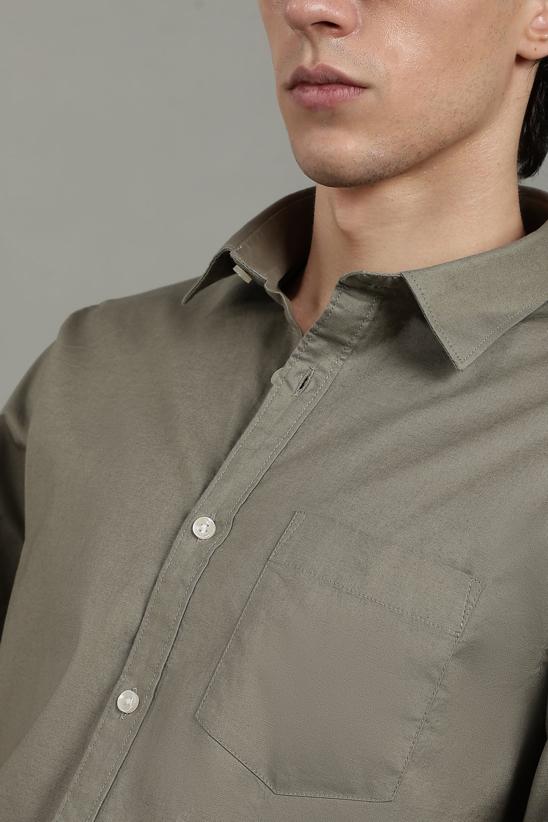 Close-up of a man  wearing a sage green button-up shirt against a gray background
