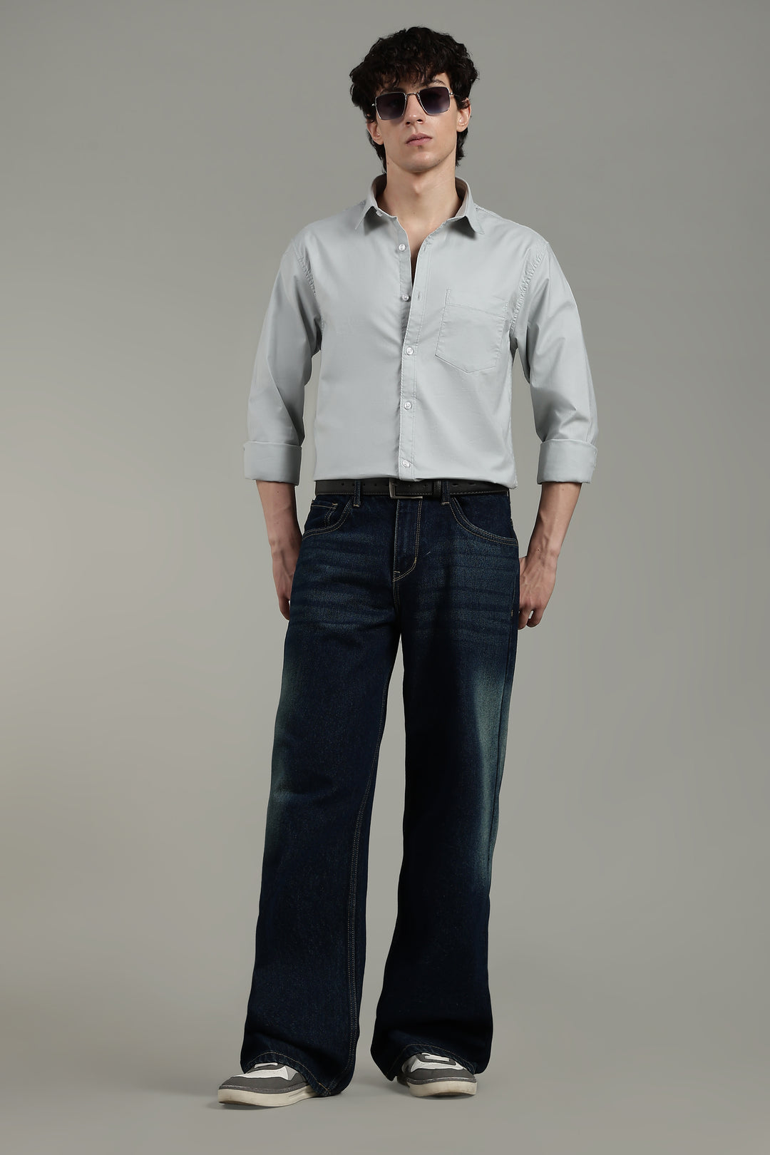 man wearing a icy blue shirt and dark blue jeans on a plain background