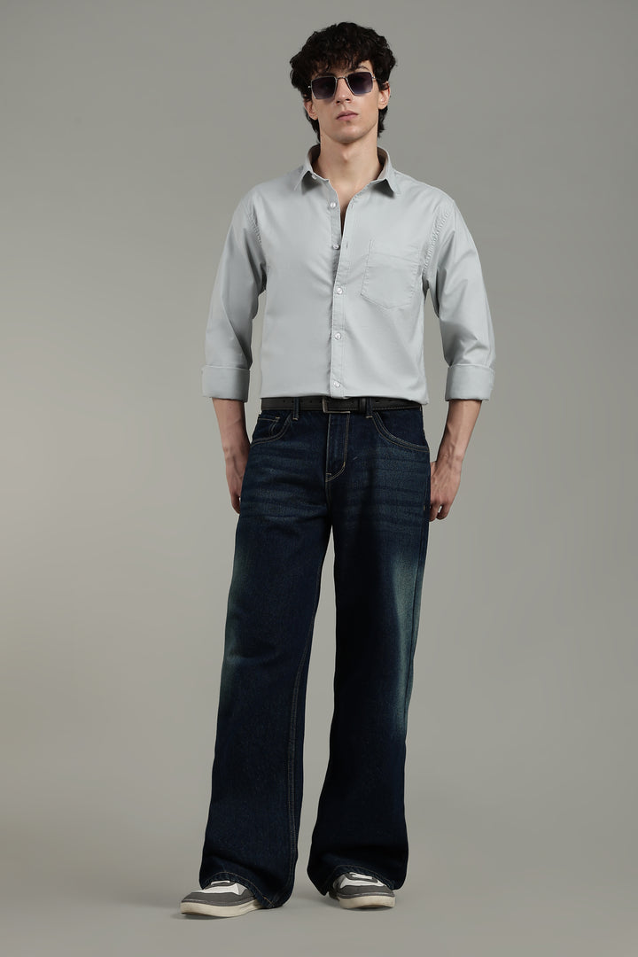 man wearing a icy blue shirt and dark blue jeans on a plain background