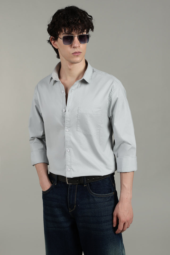 Man wearing a icy blue button-up shirt and dark jeans against a plain background