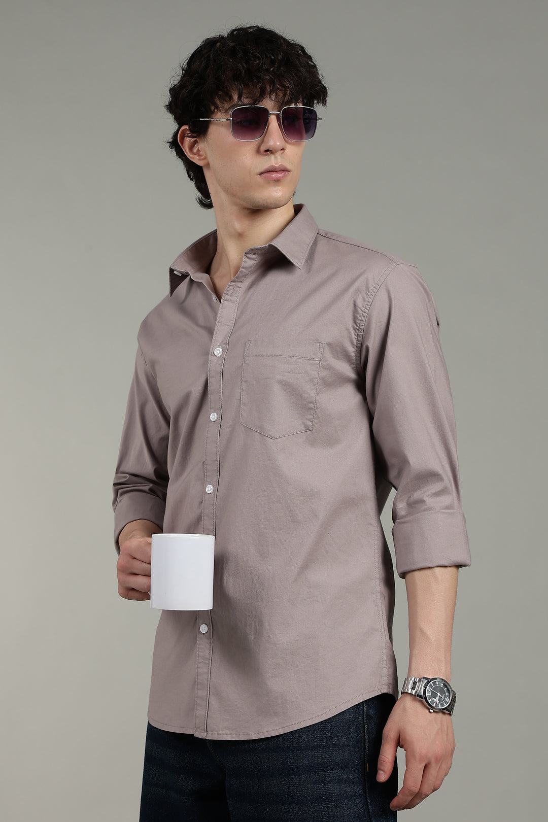 Man wearing a light mink shirt and sunglasses, holding a white mug against a gray background