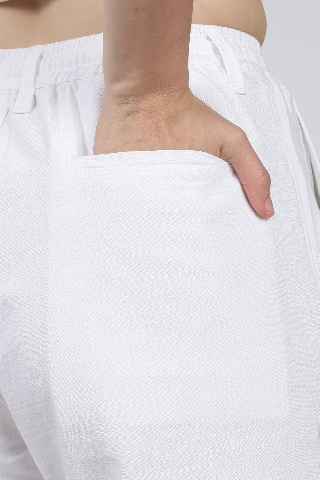 woman wearing white pants with a hand on the waist against a plain background