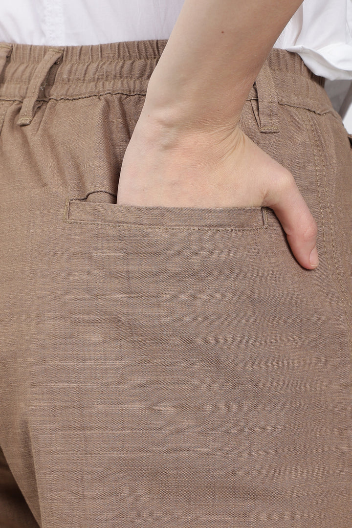 Close-up of brown pants with a hand in the pocket, wearing a white shirt.