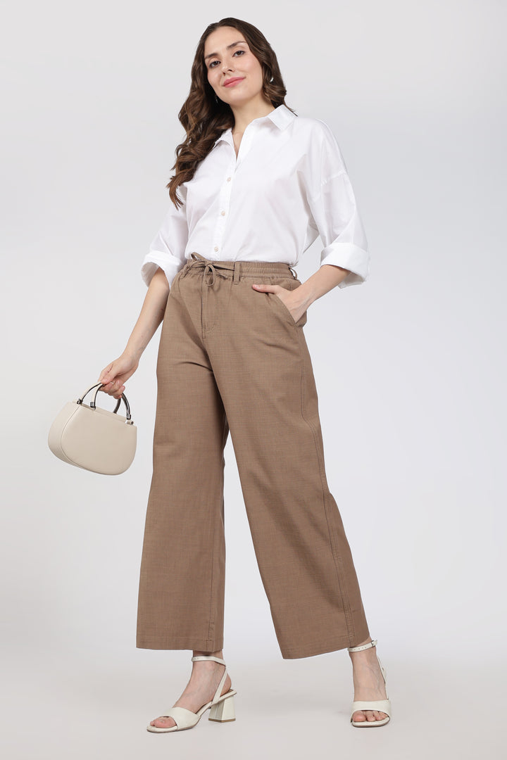 Woman wearing a white shirt and brown pants with a beige handbag on a white background